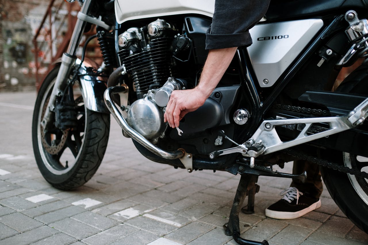Close-up of a mechanic using a wrench to tighten a part of a motorcycle engine outdoors.